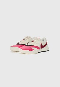 Athletic sneakers featuring a cream upper with pink and red accents, textured overlays, and black rubber outsole. Laces and padded collar included.
