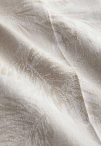 Tissu crème avec des motifs discrets de feuilles de palmier en relief, créant une surface texturée et ondulée.