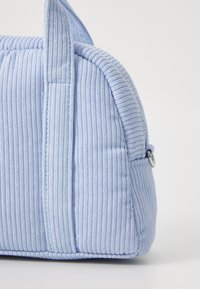 Sac en velours côtelé bleu avec une texture à côtes verticales, forme arrondie et anses courtes. Présente une fermeture éclair et un accent en métal argenté.