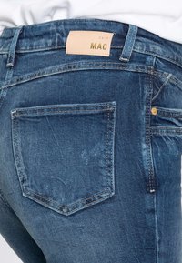 Jeans z denimu v středně modré barvě s texturovaným povrchem. Obsahují koženou nášivku s embosovaným textem a designem jednokapsy na zadní straně.