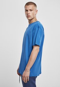 Tricou din bumbac albastru cu o croială lejeră, mâneci scurte, guler rotund și tiv drept. Textură netedă cu detalii minime de cusături.
