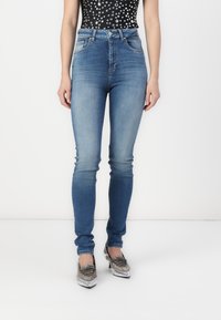 Jeans de mezclilla azul de tiro alto con un corte ajustado, que presentan un lavado desgastado, diseño de cinco bolsillos y detalles en hardware plateado.