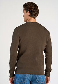 Suéter marrón de canalé con cuello redondo, mangas largas y dobladillo ajustado, combinado con jeans de mezclilla azules.