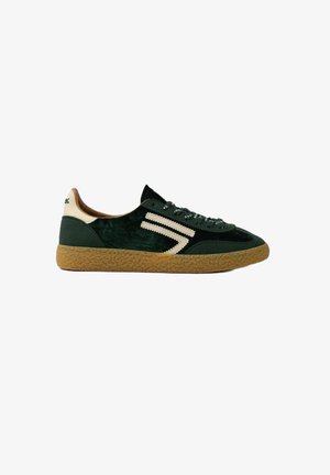 Baskets en daim vert avec des accents crème, semelle en caoutchouc texturé et lacets bicolores. Présente un design zigzag distinctif sur le côté.