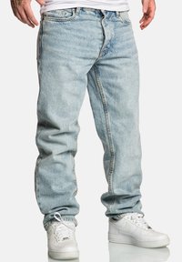 Jasnoniebieskie dżinsy o luźnym kroju, z pięcioma kieszeniami i kontrastowymi przeszyciami, w połączeniu z białymi tenisówkami.