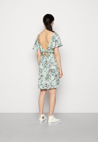 Vestido com padrão floral em verde menta, com costas em V profundo, mangas curtas e esvoaçantes, e cintura ajustada, combinado com ténis brancos de cano alto.