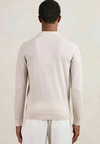 Helle beige Langarm-Polohemd mit strukturiertem Finish, klassischem Kragen und gerippten Bündchen, kombiniert mit gestreiften weißen Hosen.
