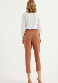 Bruine op maat gemaakte broek met een gladde textuur, middelhoog taille, taps toelopende benen en een cropped lengte, gecombineerd met een wit overhemd met lange mouwen.