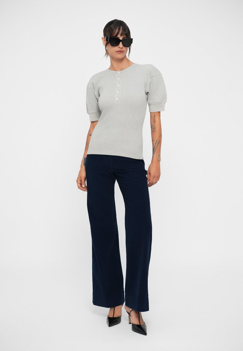 Gray ribbed short-sleeve top with button placket, paired with navy wide-leg pants and black pointed-toe heels on a plain background.