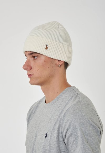Berretto a coste bianche con risvolto e piccolo logo ricamato. Il modello indossa una maglietta grigia con collo tondo, vista di lato.