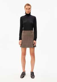 Zwarte lange mouwen coltrui gecombineerd met een bruin corduroy mini-jurk. Het model draagt zwarte gestifte instappers. Eenvoudige witte achtergrond.