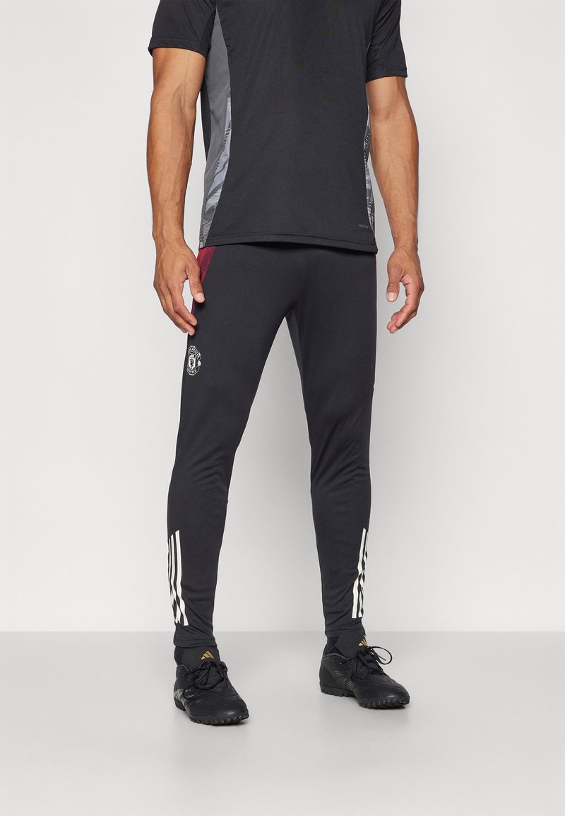 Sorte atletiske bukser med en tætsiddende design, der har hvide striber på siderne og et logo på låret. Fremstillet af strækbart stof.