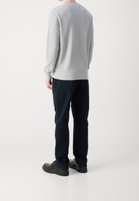 Hellgrauer Sweatshirt mit strukturiertem Finish, Rundhalsausschnitt und gerippten Bündchen, kombiniert mit dunkelblauen Hosen und schwarzen Schuhen.