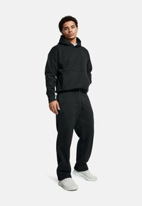 Črn komplet hoodieja in trenirk iz mehkega materiala. Hoodie ima kenguru žep; trenirke imajo vrvico in stranske žepke.