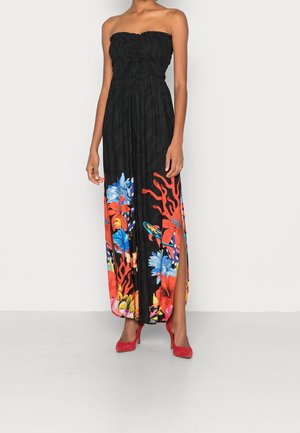 Robe longue noire sans bretelles avec motifs floraux et coraux colorés, fente latérale, portée avec des talons hauts rouges sur un mannequin debout.