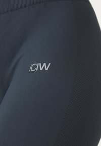 Sötétkék sportleggings sima textúrával és bordázott derékpánttal. Ezüst „ICIW” logóval rendelkezik, és légáteresztő hálós panel található rajta.