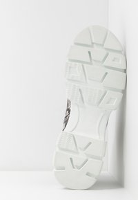 Czarny i szary wzorzysty bieżnik buta sportowego z białą gumową podeszwą. Posiada teksturowane uchwyty oraz wyprofilowany kształt zapewniający przyczepność.