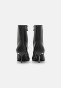 Zwarte leren enkelboots met een gladde textuur, slanke stilettoten en ritsen aan de achterkant voor sluiting. Heeft een strakke, minimalistische uitstraling.