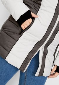 Giacca imbottita con esterno bianco e grigio scuro. Presenta polsini neri a coste, tasche laterali con zip e un dettaglio della cerniera in contrasto.
