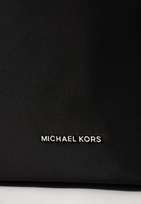 Borsa tote in tessuto nero con texture liscia, caratterizzata dal logo "MICHAEL KORS" in tonalità argento. Design semplice senza ulteriori accenti o motivi.