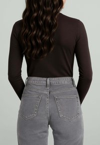 Maglietta marrone a maniche lunghe abbinata a jeans grigi a vita alta con tasche posteriori e texture sfumata, vista da dietro.