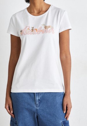 Femme portant un t-shirt blanc avec un texte rose pastel et de petites illustrations de chiens, associé à un pantalon cargo en denim bleu.
