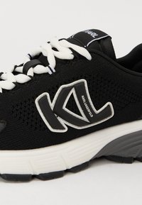 Black athletic shoe with mesh upper, white accents, thick sole, and prominent "KL" logo. Features round laces and a padded collar.