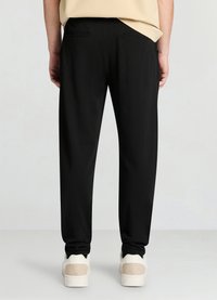 Black tapered trousers with a smooth texture, featuring two back pockets and a mid-rise waist, paired with white sneakers.