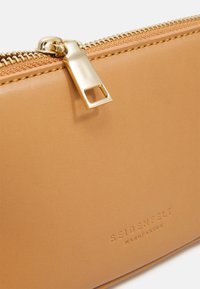 Vihreä nahkainen lompakko, jossa on kultaiset vetoketjukiinnikkeet, kohokuvioitu logo ja sileä pinta. Ominaisuuksiin kuuluvat siistit linjat ja minimalistinen muotoilu.