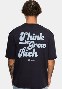 Marineblå oversized t-shirt med stor lys bl�å tekst, der står "Tænk og Bliv Rig" på bagsiden, lavet af bomuldsstof.
