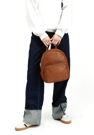 Brun læder rygsæk med tekstureret finish, afrundet design, håndtag i toppen, lynlås lomme foran, båret med oversized denim og hvide sneakers.