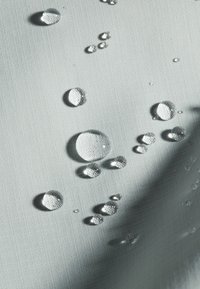 Gestructureerde lichtgrijze stof met waterdruppels van verschillende groottes op het oppervlak, die de vochtbestendigheid en glans benadrukken.