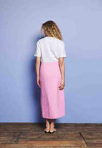 Λευκό κοντομάνικο μπλουζάκι συνδυασμένο με ροζ, υφασμάτινη, φούστα μέχρι τους αστραγάλους. Ξύλινο δάπεδο και ανοιχτό μπλε τοίχος στο φόντο.