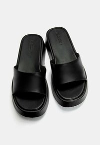 Black platform sandals made of matte leather with a wide crossover strap and a smooth sole. Features a contoured footbed for comfort.