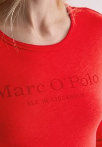 Rotes T-Shirt aus weichem Stoff mit Rundhalsausschnitt. Mit dem Aufdruck 'Marc O'Polo' und 'EST. IN STOCKHOLM' in einer dunkleren Farbstufe.