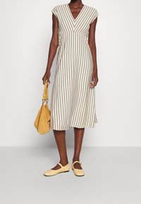 Pruhované béžové šaty s výstřihem do V, krátkými rukávy a splývavým A-liniovým střihem. Spárovány s hořčicovou kabelkou a světlými žlutými balerínami.