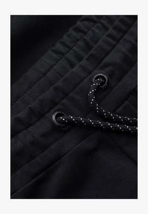 Tessuto nero con una superficie texturizzata, caratterizzato da una vita arricciata e lacci neri infilati attraverso occhielli opachi.