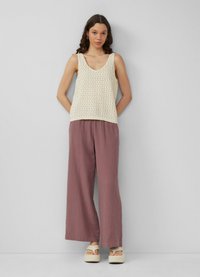 Haut sans manches en tricot ivoire avec un décolleté en V et un motif en tissage ouvert, associé à un pantalon large en rose poussiéreux et des sandales à plateforme.
