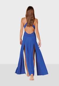 Dlhé modré šaty s otvoreným chrbtom, vysokými rozparkom na oboch stranách a priliehavým telom. Vyrobené z hladkej, prúdiacej látky.
