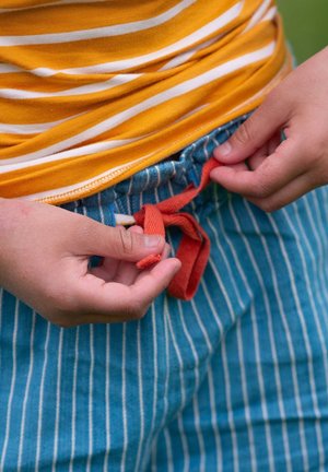 Child's outfit showing a yellow-striped shirt and blue vertically striped shorts. Red drawstring being tied by hands.