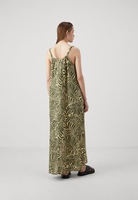 Maxikjole i et grønt og beige bladmønster, med justerbare spaghettistropper og en løs, svakt flytende silhuett. Stoffet virker glatt.