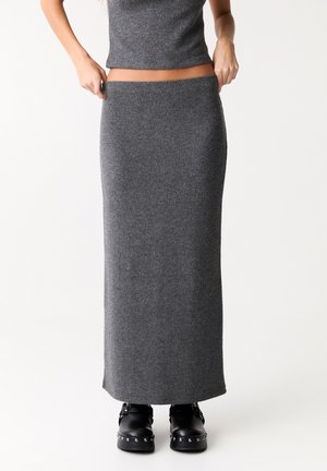 Grauer, gestrickter Maxirock mit einem figurbetonten Bund und geradem Schnitt, kombiniert mit schwarzen Clogs mit metallischen Nieten.