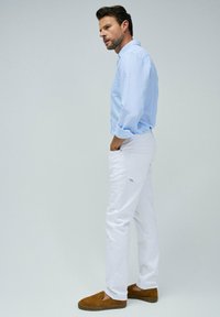 Camicia a maniche lunghe azzurro chiaro, pantaloni bianchi e mocassini marroni. La camicia presenta una tasca; i pantaloni hanno tasche laterali e posteriori.