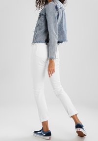 Jeansjacka med en kortad design och fransad fåll, i kombination med vita tajta byxor och marinblå sneakers med vita accenter.