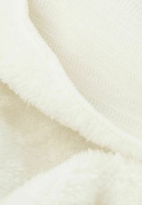 Vit plyschfilt med en mjuk, strukturerad yta med växlande släta och fluffiga sektioner, vilket skapar en mysig lager-effekt.