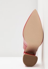 Chaussure à talon haut rouge, inclinée vers le haut, montrant la semelle texturée et le marquage de taille 37, posée sur des surfaces blanches.