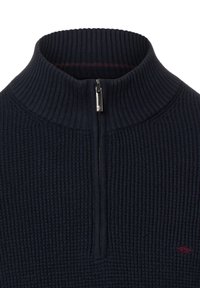 Marineblauer Strickpullover mit hohem Kragen und einem Reißverschluss bis zum Viertel; strukturierte Oberfläche und ein kleines rotes Logo auf der Brust.