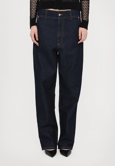 Jeans largi din denim albastru închis cu cusături portocalii, talie înaltă și buzunare frontale. Asortați cu pantofi cu vârf ascuțit negri și un top tricotat texturat.