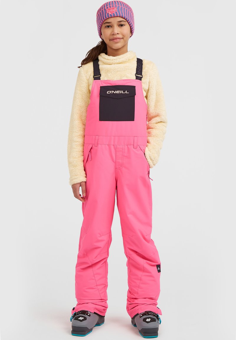 Roze sneeuwoverall met verstelbare banden, een zwarte voorkantzak en een zachte beige fleece top. De outfit is gecombineerd met sneeuwlaarzen en een gestreepte muts.