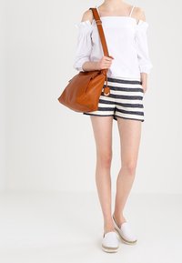 Blusa bianca senza spalle, pantaloni corti a righe blu navy e bianchi, borsa a tracolla color sabbia e espadrillas bianche con suole in juta. Design semplice.